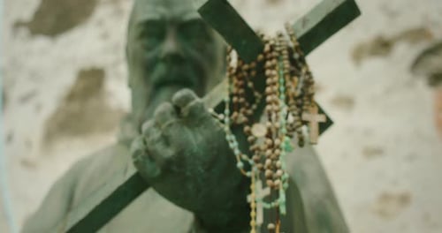 Rosarycovered Cross Held By Statue with Solemn Face and Stone Wall Background