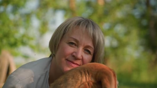 CloseUp of Woman Smiling Beside Her Brown Dog in Lush Green Setting