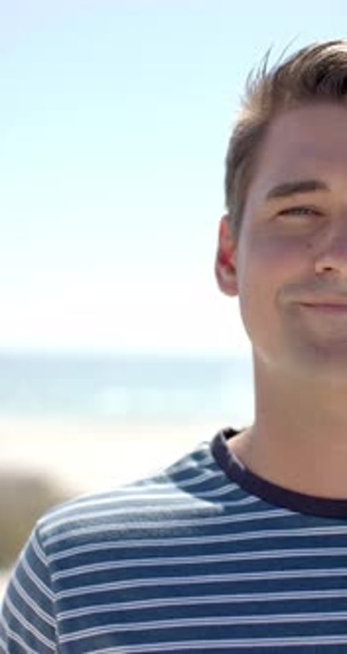 Vertical video: Smiling man enjoying sunny day at beach, wearing striped shirt