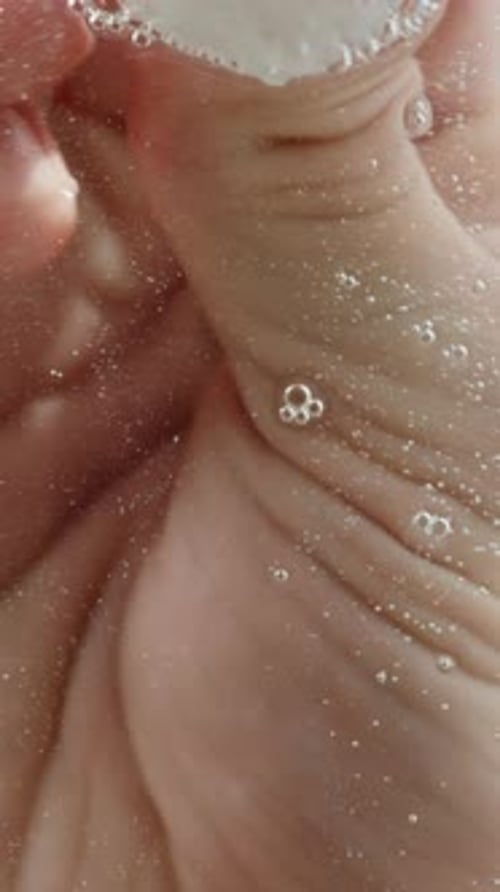Vertical video. I wash the glass on a blue background, low-angle view from below. Water bubbles.