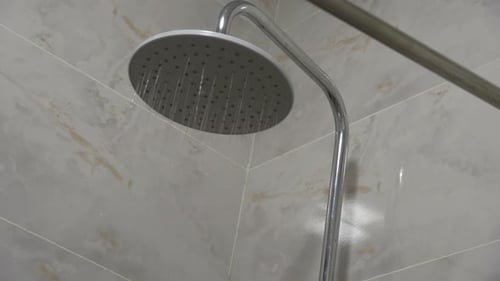 Water Flowing from Modern Shower Head in Bathroom