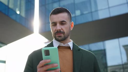 Low Angle Young Caucasian Man in Formal Wear Standing in Front Office Building Looking Cell Phone
