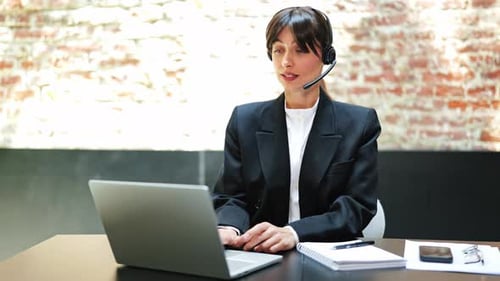 Businesswoman in Headset Works on Laptop and Speaks at Online Meeting in Office