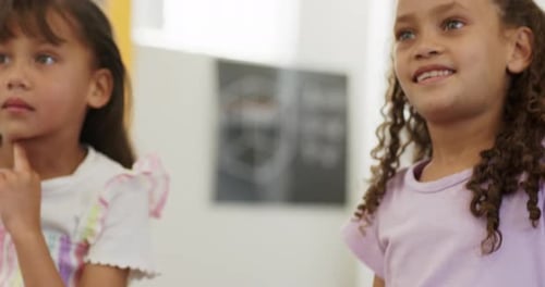African American child girls sitting in classroom responding to teacher, raising hand near tablet
