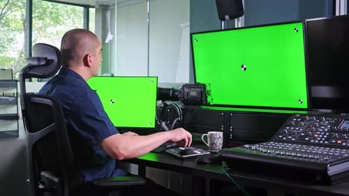 Male video editor works with software on chroma screens then stands up