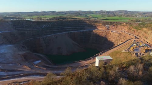 Open Pit Quarry Mining Landscape with Heavy Machinery Working Around Deep Excavation and Water