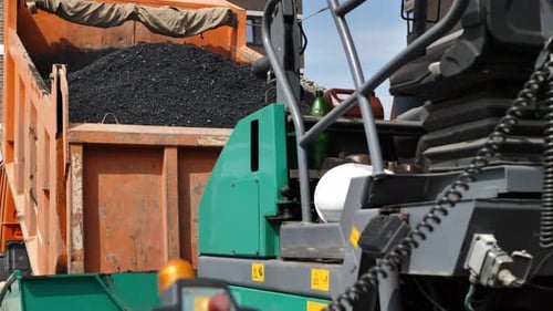 Construction of a New Road a Truck Pours Hot Asphalt Into the Bucket of an Asphalt Paver