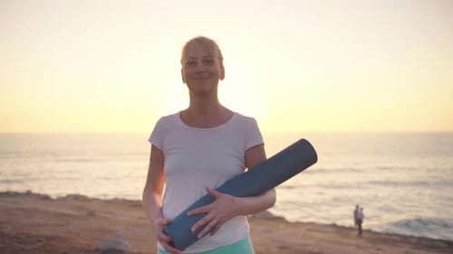 Mature Woman Holding Yoga Mat Ocean Background at Sunset