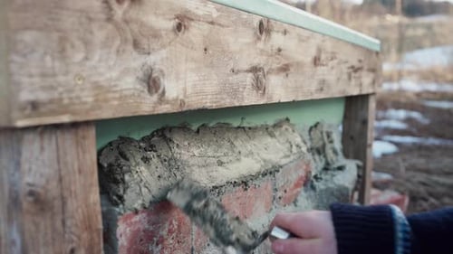 Worker With Trowel Putting Mortar Paste On Top Of Brick Stones. - close up shot