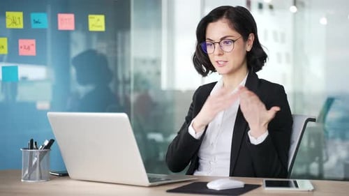 Frustrated female professional arguing during video call at office desk. Businesswoman expressing