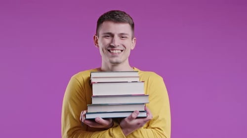 Young Male Student Holds Stack University Books From College Library on Pink