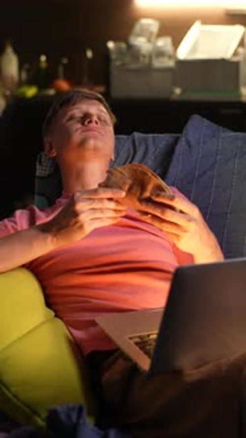 Vertical Portrait of Happy Young Man Eating Tasty Taco Burger and Watching Movie on Laptop Resting