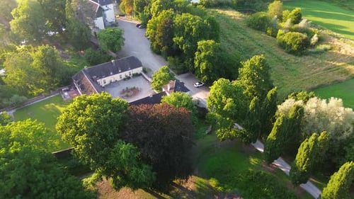 A charming historic estate with a U-shaped courtyard, surrounded by lush greenery, fields, and trees