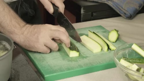 Hands cut a green zucchini in kitchen with boiling water close up, sharp knife