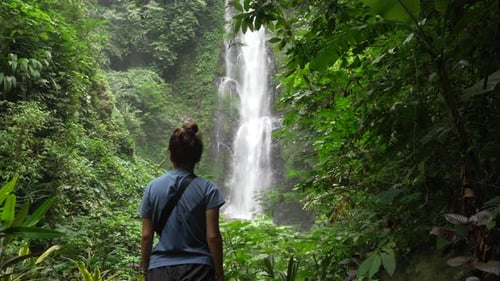 Young woman faces Melanting Waterfall in tropical jungle, Munduk, Bali. Indonesia. A popular tourist