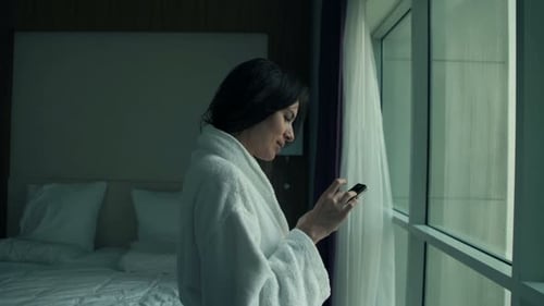 Woman in bathrobe uses phone in hotel room