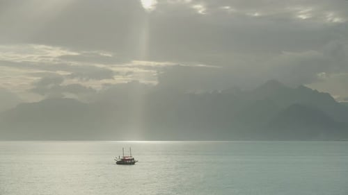 A sunbeam through the clouds acts like a spotlight, illuminating the path of a boat sailing.