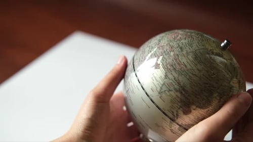Die Hand dreht einen grauen Globus und wählt einen zufälligen Punkt auf der Weltkarte aus
