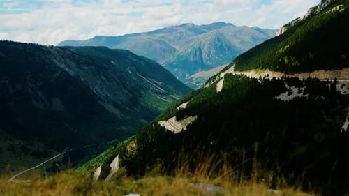 Die kurvenreiche Bergstraße erstreckt sich durch üppige grüne Täler mit fernen Gipfeln unter blauem Himmel