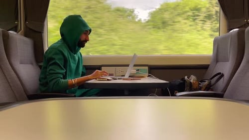 Man In Green Hoodie Using Laptop On Train While On The Trip. - wide