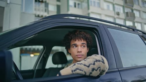 Young Adult Sits in a Car by Apartment Building