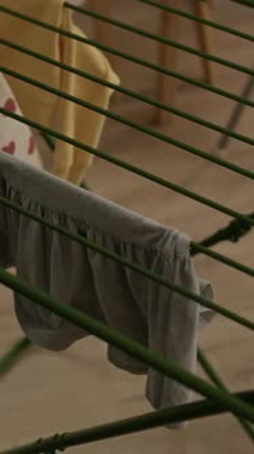 Vertical of Hands of Black Mother Hanging Baby Laundry on Rack at Home