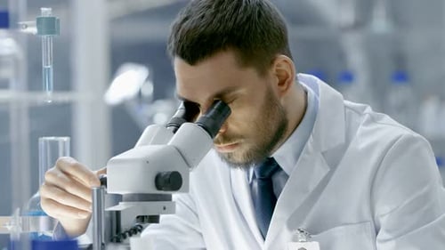 Research Scientist Looks into Microscope. He's Working in a High-End Modern Laboratory with Beaker