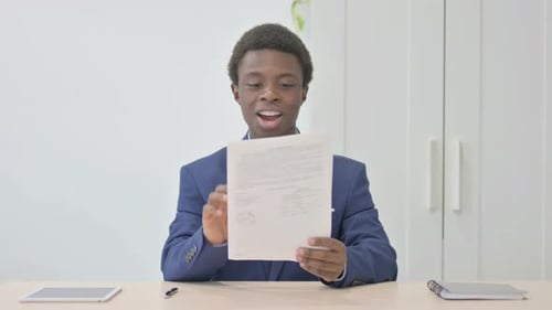Young African Businessman Celebrating Success while Reading Documents in Office