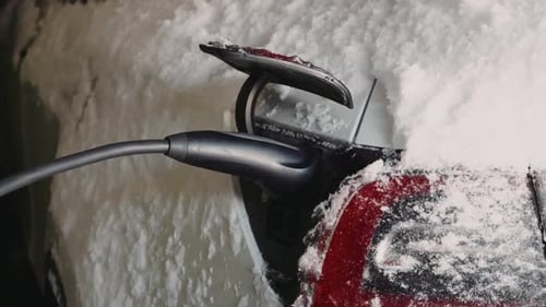 Closeup of electric car charging port with cable plugged in during winter snow