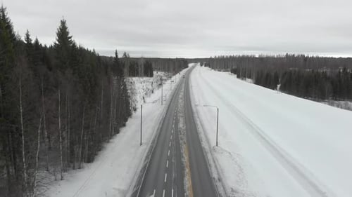 Aerial, drone shot, over a small truck, on road 6, surrounded by snowless trees, on a cloudy, winter