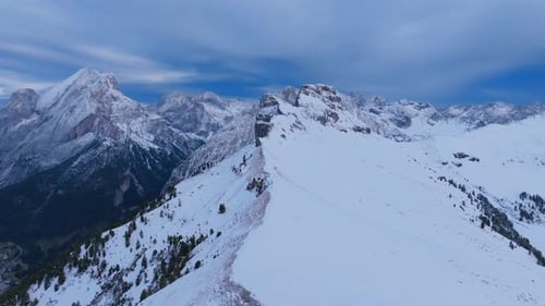 Aerial footage flying over the ride of the peak of a mountain that is covered in snow outside the to