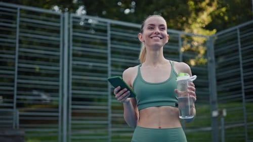 Fit Woman with Phone and Water Bottle Outdoors
