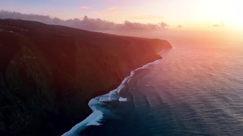 Sunset over a rugged coastline with rolling waves and dramatic cliffs