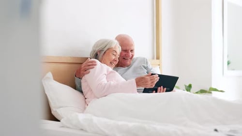 Loving Senior Couple Relaxing in Bed with Tablet