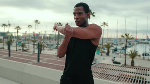 Young Man Stretching Before a Workout by the Marina
