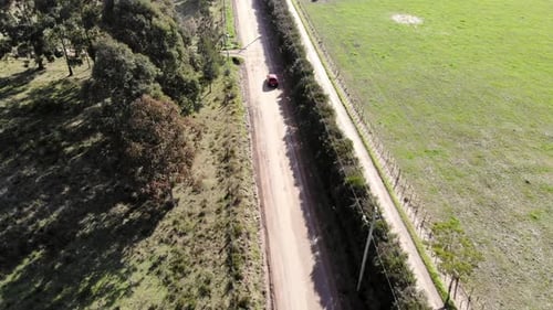 Aerial shot of car driving on road in a countryside with dirt street. Drone shot of gravel road and