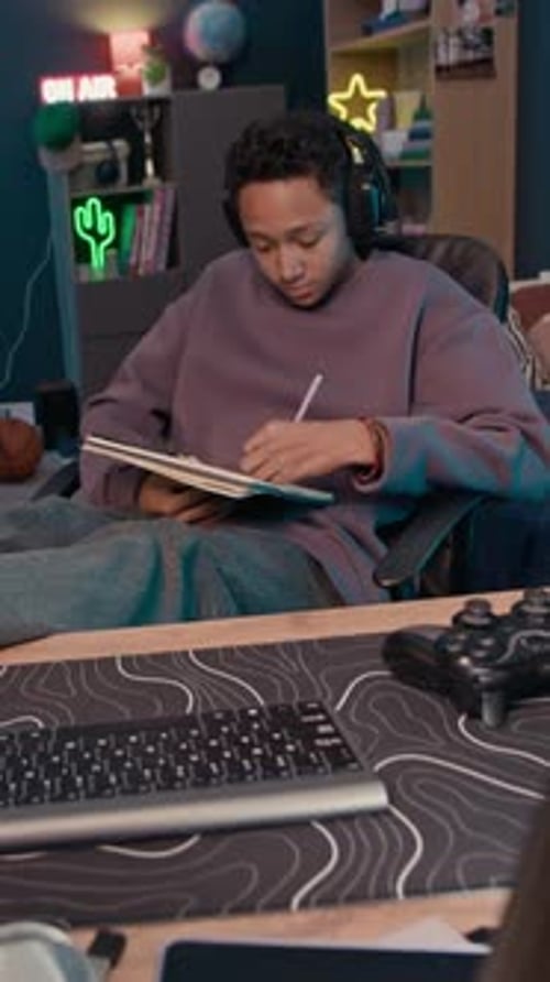 Teen with headphones writing in a notebook indoors