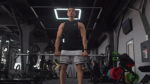 Attractive man of athletic build trains in gym doing squats with barbell, front view. Male bodybuild