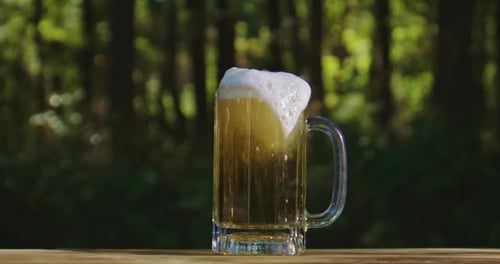 Beer Mug with Frothy Foam on Wooden Table Outdoors Refreshing Golden Beverage Glowing in Sunlight