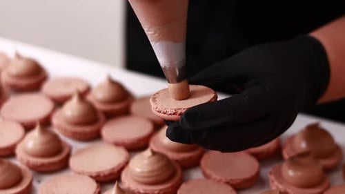 Making french desert macarons. Chef hands in black gloves with confectionery bag add cream to the