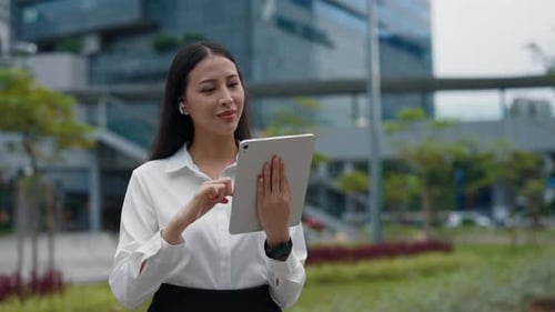 Asian Female In Business Attire Standing On The Street And Checking Her Tablet