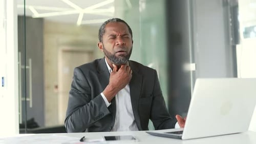 Man in Office Rubbing Throat in Pain