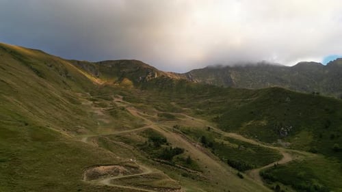 DRONE SHOT of a valley in the mountains with a road up to the hills with a cloudy sky