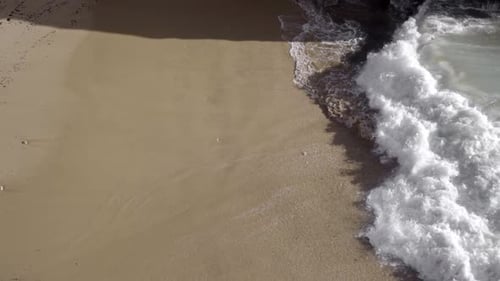 An aerual view of a wave coming to the beach in slow motion