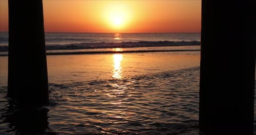 Golden sunrise reflected on surface of water as waves was onto the beach near wooden fishing pier. Q