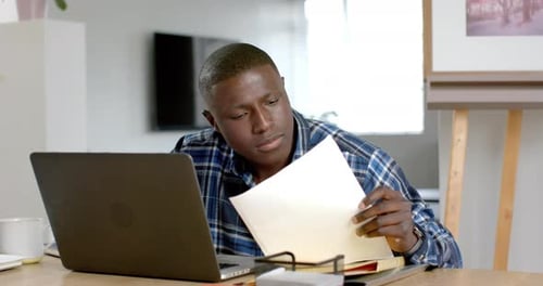 Young Adult Works at Laptop with Documents