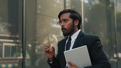 Businessman Eating Lunch Sandwich, Holding Laptop