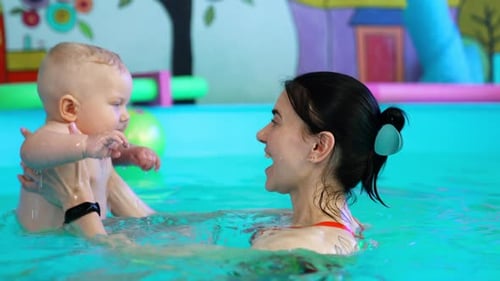 Blond baby splashing his hands cheerfully in the swimming pool.