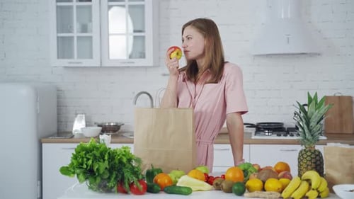 Woman Enjoying Fresh Apple in Bright Kitchen
