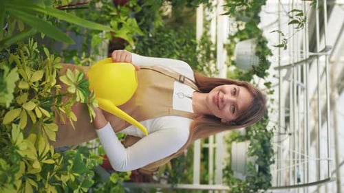 Woman Smiles with Watering Can in Greenhouse